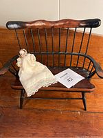 Miniature bisque doll seated on miniature Windsor style wooden settee, showing scale and overall condition of both items.