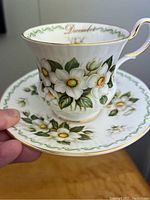Close view of teacup and saucer showing detailed Christmas Rose flower pattern, gold accents and 'December' inscription.