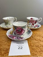Lot of three Royal Albert bone china tea cups and saucers with floral designs, arranged on a table photographed from front