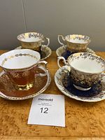 Four Royal Albert teacups with matching saucers showing diverse gold-accented series in blue, brown, and white tones, no damages visible.