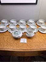 Full set of 10 teacups and saucers plus creamer and sugar bowl arranged on a table showing overall condition and quantity