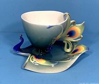 Porcelain teacup and saucer with peacock design, showing front left angle.