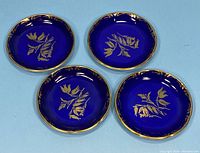 Photo showing four round cobalt blue Aynsley coasters with gold floral designs and gold-bordered edges arranged together.