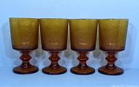 Front view of 4 amber Indiana Glass vintage stemmed glasses with textured tree bark design on bowl and faceted stems.