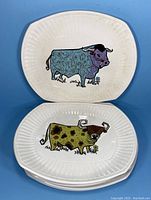 Set of seven rectangular ironstone plates with colorful stylized bulls, some stacked showing two designs clearly.