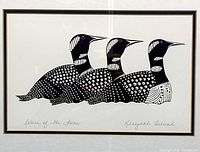 Close-up photo of the lithograph artwork showing three stylized loons in black and white with red eyes, signed and titled in pencil on the lower margin.