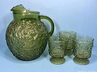 Full set view showing green textured pitcher with handle alongside three matching pedestal glasses on white background