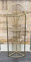 Front view of the full brass tone metal 4-tier corner plant stand showing the arched top and four shelves designed to fit a corner.