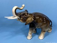 Front right three-quarter view of brown and ivory porcelain elephant figurine with raised trunk and detailing.