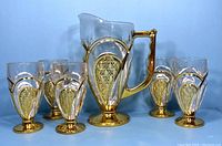 Full set of one pitcher and six glasses with gold pineapple pattern on clear glass, displayed against a blue background.