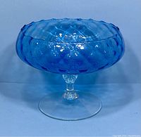 Front view of vintage blue glass pedestal bowl with textured pattern and scalloped rim on a clear base.