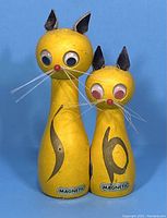 Front view of vintage yellow wooden cat salt and pepper shakers, showing both sizes, facial details, and magnetic labels
