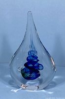 Front view of clear teardrop paperweight showing internal blue spiral ribbon with green accents and air bubbles.