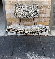 Front view of vintage mid-century modern lounge/accent chair showing the spotted upholstery on the seat and backrest, metal frame, and three legs visible due to the angle.