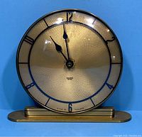 Full frontal view of the vintage Smiths Setric mantle clock showing the gold textured dial, black numerals, and brass-tone base against a blue background.
