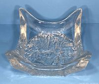 Front angle view of a clear art glass bowl with textured base and upward curved corners on a blue background.