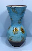 Side view showing hourglass form and blue glaze with brown and yellow abstract accents.
