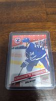 Close up photo of Auston Matthews Canadas Rookies hockey card in plastic protective case on a wood floor background.