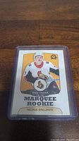Photo shows a Brady Tkachuk Marquee Rookie hockey card in a clear protective plastic case on a wooden surface.