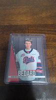 Photo of Connor Bedard 2023 Hot Shot Prospects pre-rookie hockey card in protective case on wooden surface.