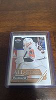 Hockey trading card of Connor McDavid in protective plastic sleeve, showcasing the player in white Edmonton Oilers uniform with the All-Star Parkhurst branding.