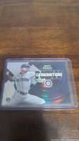 Front view of Matt Brash rookie card in plastic sleeve on wooden surface showcasing player pitching in Mariners uniform, with Generation Now design and holographic accents.