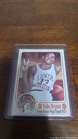 Photo of basketball trading card featuring Kobe Bryant in Lower Merion High School uniform, in plastic card protector.