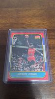 Photo of Michael Jordan rookie reprint card in protective plastic case on wooden surface