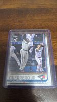 Photo of Vladimir Guerrero Jr. rookie card featuring him in white Toronto Blue Jays uniform making a play, in clear protective plastic casing on wooden surface.
