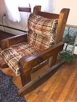 Single child-sized wooden Mission style rocking chair with brown beige plaid cushion sitting on a wooden floor.