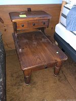 Two step up trestle end tables made of wood, showing the upper tier with three small drawers with round knobs and lower tier flat surface. Tables are medium brown with natural grain visible and some wear.