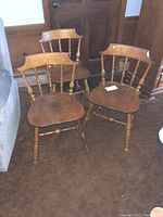 Three vintage wooden Nichols & Stone dining chairs arranged together on brown carpet near wooden door and wall with part of blue couch visible