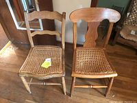 Two antique wooden chairs side by side showing cane woven seats and distinct wooden backrest designs on a hardwood floor.