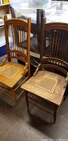 Two antique wooden dining chairs with cane seats, different wood colors and designs shown from front angle.