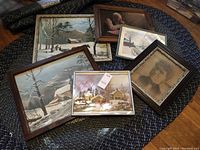 Six assorted framed pictures including five winter landscapes and one portrait of elderly man, arranged on a fabric surface.
