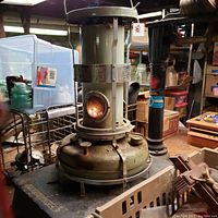 Side view of the Aladdin Blue Flame heater showing the metal body, base fuel tank, and flame window with lit flame inside.