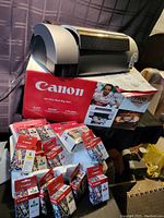 Canon i9900 photo printer placed on top of original box with many unopened Canon ink cartridge boxes spread around.