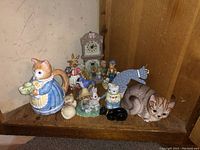 Assorted cat and animal figurines including damaged cat teapot and small perfume bottles on shelf corner.