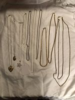 Photo showing 10 necklaces laid flat on white fabric, highlighting variety of pendants and chain styles in silver and gold tones.