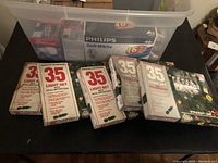 First photo showing multiple boxes of 35-light Christmas light sets and Philips soft white light bulb packs inside a clear plastic bin.