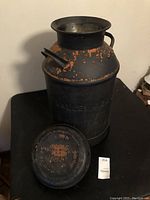 Photo showing the milk can with removable lid placed in front, highlighting embossed lettering and paint wear.