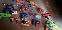 Multiple Nerf and toy dart guns arranged on floor showing variety of colors, styles, and models.