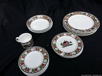 Full set view showing stacked bowls, plates, saucers, and the coffee cup with a colorful quilt and barn pattern border.