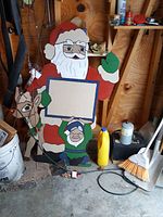 Painted wooden Santa figure about 4 feet tall holding a blank sign, with a reindeer and an elf figure at its base, displayed in a garage setting.