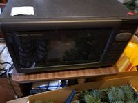 Front view of Sharp Carousel microwave placed on a wooden surface, showing the large viewing window and black housing.