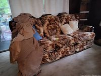 Sofa with floral upholstery covered by fabric slipcover with cushions and draped cloth on one arm, placed in a living area.
