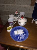 Top view of blue and white Spode cream and sugar set, snowman mug, Roayl Norfolk plate and multiple mugs on wood surface