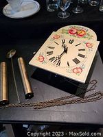 Dial of custom toleware clock with floral and fruit designs, pendulum weights, rod and chains beside it