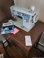 Light blue vintage Brother sewing machine placed on wooden table along with original user manual and pink note.