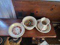 Vintage floral ceramic pitcher and bowl set on wooden bench with other items.
